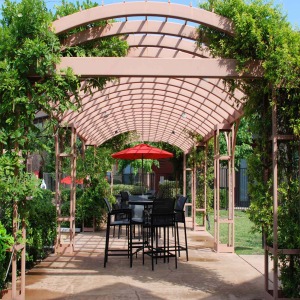 Pergola near the pool area with lush landscaping and tall bistro table, chairs and umbrellas