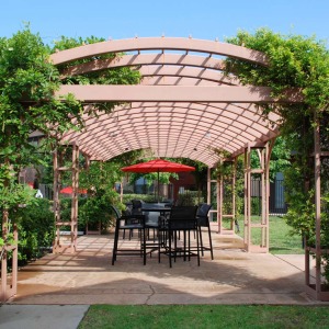 Pergola near the pool area with lush landscaping and tall bistro table, chairs and umbrellas